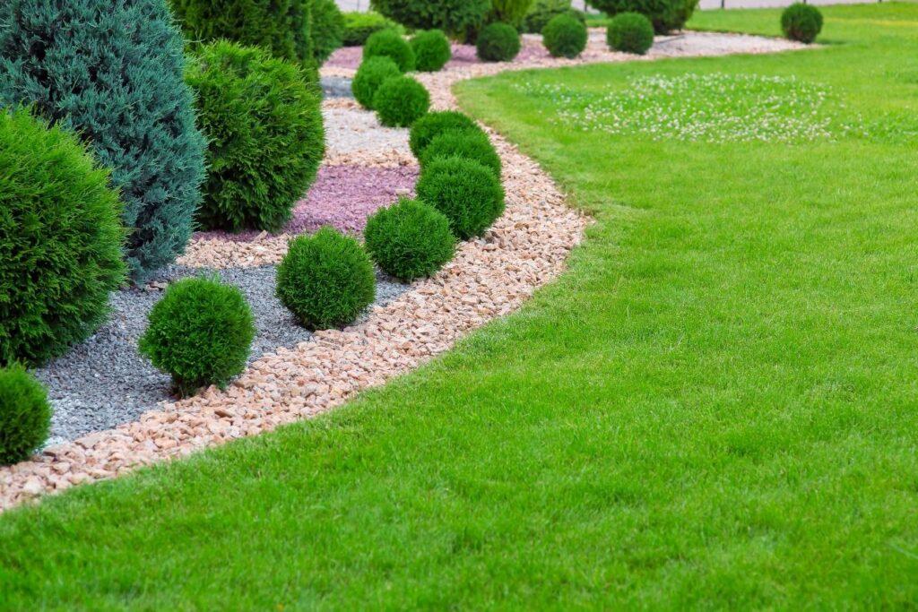 Ein Garten mit geschwungenen Beeteinfassungen aus bunten Ziersteinen und gepflegtem Rasen für eine harmonische Optik.