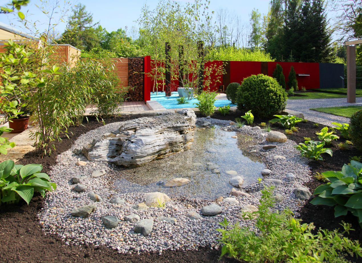 Ein Wassergarten mit Ziersteinen, Natursteinfelsen und üppiger Bepflanzung – eine moderne und entspannende Gartengestaltung.