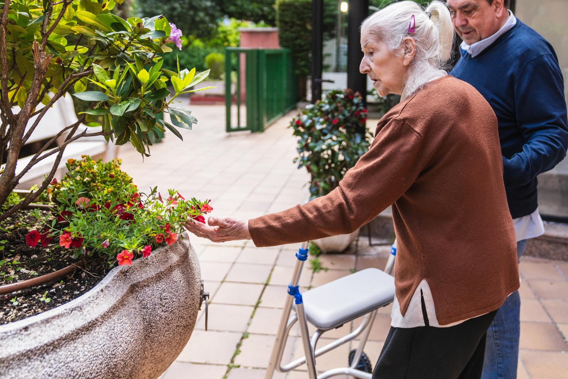 Seniorin mit Begleitung betrachtet Blumen im Innenhof | Pflegehilfskraft Frankfurt